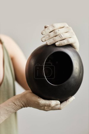 Foto de Primer plano de talentosa artista femenina sosteniendo vasi de cerámica hecha a mano en negro - Imagen libre de derechos