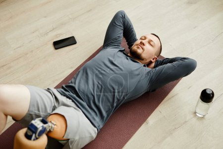 Foto de Vista superior del hombre con la pierna protésica haciendo ejercicios en casa en la esterilla de yoga - Imagen libre de derechos