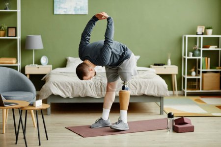 Téléchargez les photos : Portrait complet de l'homme avec la jambe prothétique travailler à la maison et faire des exercices d'étirement, copier l'espace - en image libre de droit
