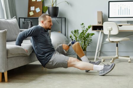 Téléchargez les photos : Portrait latéral de l'homme avec la jambe prothétique faisant des exercices à la maison dans un intérieur minimal - en image libre de droit