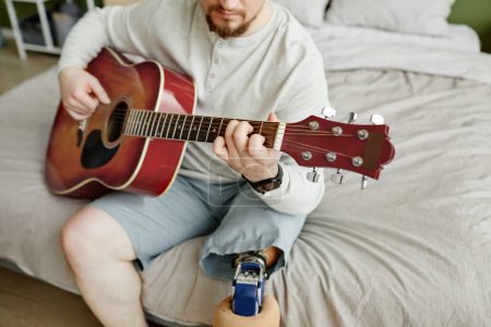 Foto de Primer plano del hombre con la pierna protésica tocando la guitarra en casa, espacio de copia - Imagen libre de derechos