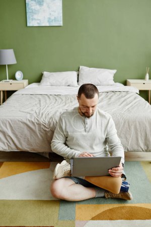 Téléchargez les photos : Portrait vertical de l'homme avec prothèse de jambe à l'aide d'un ordinateur portable assis sur le sol à la maison - en image libre de droit