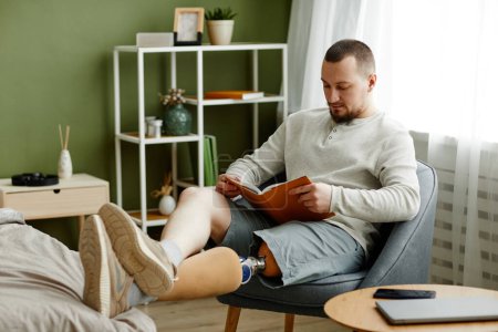 Téléchargez les photos : Portrait d'homme adulte avec livre de lecture de jambe prothétique à la maison et relaxant, espace de copie - en image libre de droit