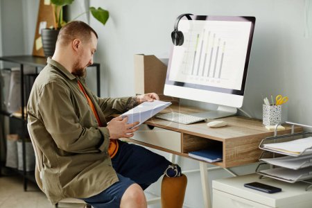 Téléchargez les photos : Portrait latéral d'un homme avec une jambe prothétique travaillant au bureau à domicile et lisant des documents, espace de copie - en image libre de droit