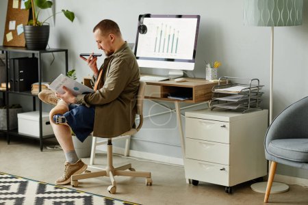 Photo for Side view portrait of man with prosthetic leg reading document at workplace in office and recording voice message, copy space - Royalty Free Image