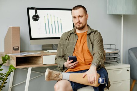 Téléchargez les photos : Portrait minimaliste de l'homme adulte avec prothèse de jambe sur le lieu de travail en regardant la caméra - en image libre de droit