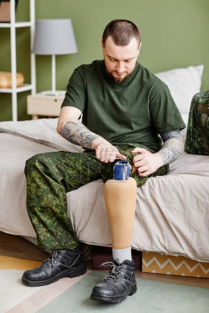 Photo for Vertical full length portrait of military veteran fixing prosthetic leg - Royalty Free Image