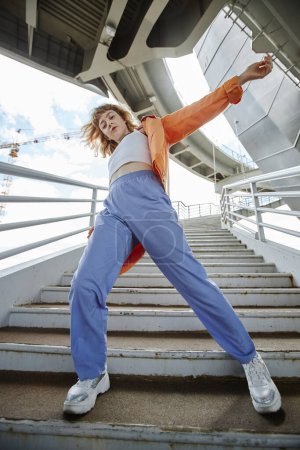 Téléchargez les photos : Plan dynamique pleine longueur d'une jeune femme dansant à l'extérieur en zone urbaine et portant des vêtements de rue - en image libre de droit