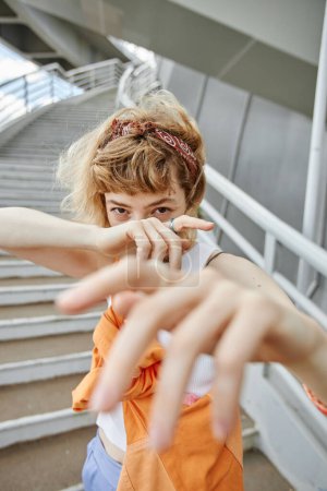 Téléchargez les photos : Portrait vertical d'une jeune femme qui pose à l'extérieur en milieu urbain et tend la main à la caméra - en image libre de droit