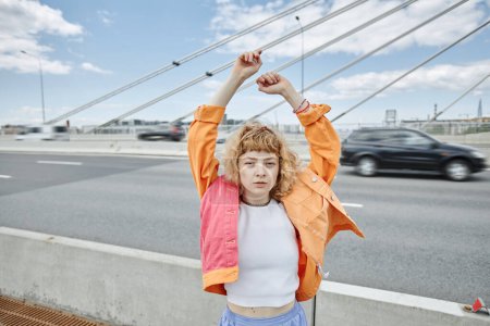 Photo for Waist up portrait of free young woman wearing colorful clothes on city bridge and looking at camera, copy space - Royalty Free Image