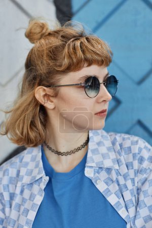 Téléchargez les photos : Portrait vertical latéral de jeune femme à la mode aux cheveux bouclés posant sur fond bleu - en image libre de droit