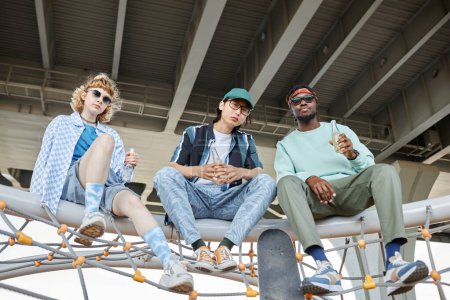 Foto de Diverso grupo de tres jóvenes pasando el rato juntos en el entorno urbano y mirando a la cámara - Imagen libre de derechos