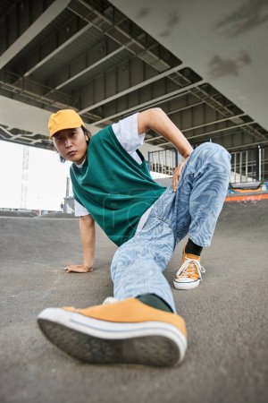 Téléchargez les photos : Fisheye de jeune homme asiatique dansant hip hop en plein air et portant des vêtements colorés de style de rue en milieu urbain - en image libre de droit