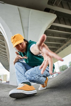 Téléchargez les photos : Fisheye de jeune homme asiatique dansant en plein air et gesticulant à la caméra portant des vêtements colorés de style de rue - en image libre de droit
