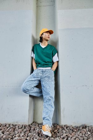 Photo for Vertical portrait of young Asian man wearing colorful street style clothes standing by concrete wall in urban setting - Royalty Free Image