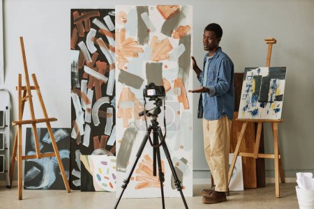Téléchargez les photos : Jeune peintre afro-américain confiant présentant sa collection et soulignant leur sujet principal lors de la diffusion en direct - en image libre de droit