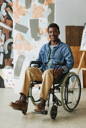 Foto de Joven artista o artesano en silla de ruedas sentado frente a la cámara en el estudio con una colección de pinturas abstractas - Imagen libre de derechos