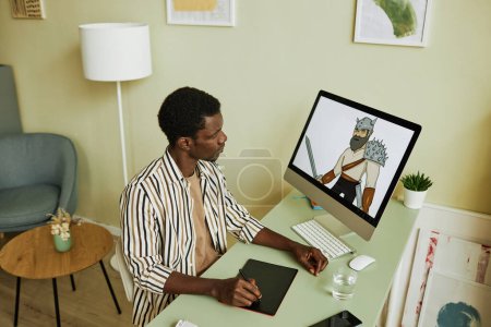 Foto de Joven diseñador gráfico creativo trabajando sobre una nueva colección de imágenes digitales mientras está sentado en el lugar de trabajo frente a la computadora - Imagen libre de derechos
