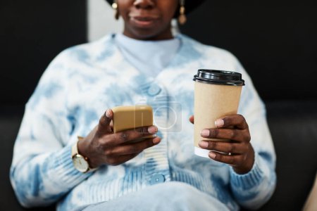 Foto de Primer plano de la joven mujer negra usando el teléfono inteligente y sosteniendo la taza de café, concepto de comunicación de la generación Z - Imagen libre de derechos