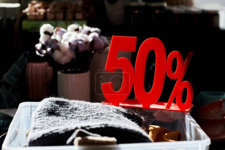 Photo for Close up of clothes bin in second hand store with 50 percent off red sale sign lit by sunlight - Royalty Free Image