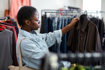 Foto de Retrato de vista lateral de una joven negra mirando ropa en una tienda de segunda mano - Imagen libre de derechos