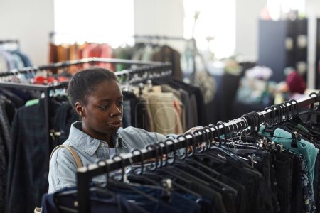 Foto de Retrato de alto ángulo de una joven negra mirando ropa en bastidores en una tienda de segunda mano - Imagen libre de derechos