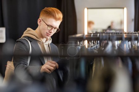 Foto de Retrato de cintura hacia arriba del joven con estilo que mira la ropa mientras compra de forma sostenible en la tienda de segunda mano, espacio para copiar - Imagen libre de derechos
