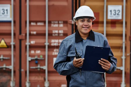 Photo for Waist up portrait of smiling female worker wearing hardhat at shipping docks with containers, copy space - Royalty Free Image