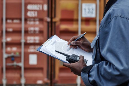 Photo for Close up of male worker wearing writing on clipboard in shipping docks with containers, copy space - Royalty Free Image