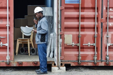 Photo for Graphic side view portrait of young male worker wearing hardhat while checking containers at shipping dock, copy space - Royalty Free Image