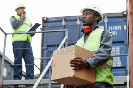 Téléchargez les photos : Portrait à la taille d'un travailleur afro-américain portant des boîtes dans les escaliers des quais d'expédition - en image libre de droit