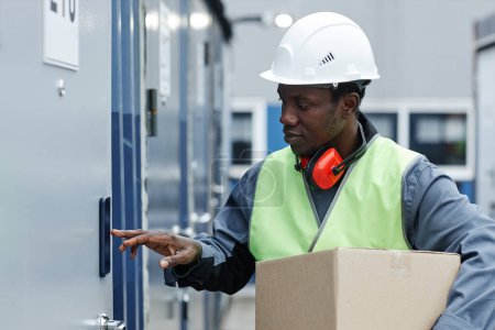 Photo for Side view portrait of black young man wearing hardhat while entering code on storage unit - Royalty Free Image