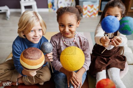 Photo for Group of adorable multicultural kids studying planets of solar system while holding their models at lesson of astronomy in kindergarten - Royalty Free Image