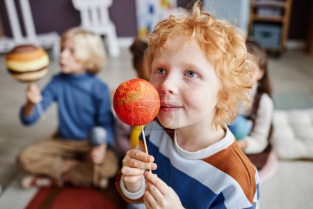 Téléchargez les photos : Adorable garçon aux cheveux roux tenant le modèle planétaire de Mars par son visage alors qu'il étudiait l'astronomie à l'école maternelle - en image libre de droit