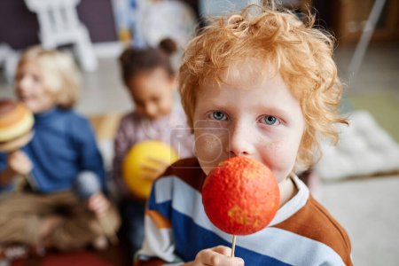 Photo for Adorable boy with ginger hair holding model of Mars planet and looking at camera while playing against other learners of nursery school - Royalty Free Image