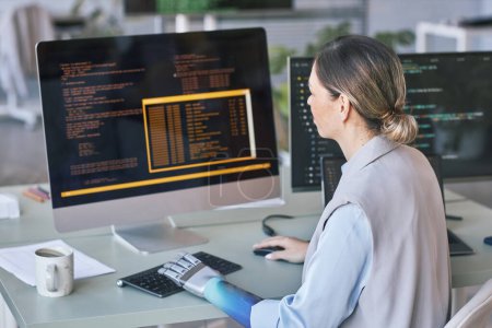 Téléchargez les photos : Programmeuse avec bras prothétique travaillant sur ordinateur dans le bureau de l'entreprise informatique - en image libre de droit