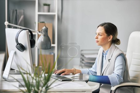Foto de Joven empresaria con brazo protésico trabajando en la computadora en la oficina - Imagen libre de derechos