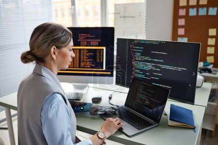 Téléchargez les photos : Jeune femme programmeur vérifier le code sur l'écran d'ordinateur portable - en image libre de droit