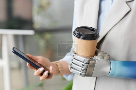 Téléchargez les photos : Image rapprochée d'une femme avec un bras prothétique tenant une tasse de café et vérifiant les notifications sur smartphone - en image libre de droit