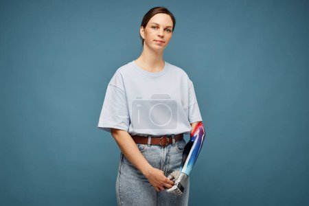 Photo for Portrait of unsmiling young woman with prosthetic arm standing against greish background - Royalty Free Image