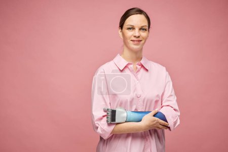 Téléchargez les photos : Portrait de jeune femme souriante avec bras bionique debout sur fond rose - en image libre de droit