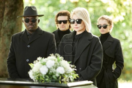 Foto de Grupo de personas vestidas de negro de pie junto al ataúd en la ceremonia funeraria al aire libre - Imagen libre de derechos