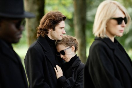 Téléchargez les photos : Portrait de jeune couple portant le deuil noir ensemble et embrassant à la cérémonie funéraire en plein air - en image libre de droit