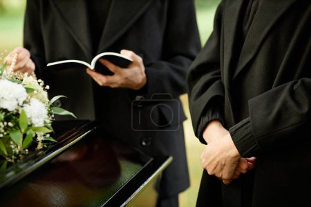 Téléchargez les photos : Femme méconnaissable portant du noir à la cérémonie funéraire extérieure avec prêtre lisant la prière en arrière-plan, espace de copie - en image libre de droit