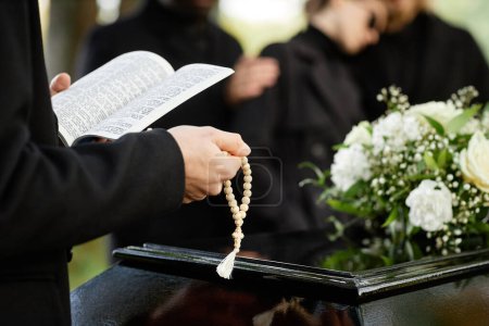 Photo for Close up of person in black praying at outdoor funeral and holding Bible with rosary, copy space - Royalty Free Image