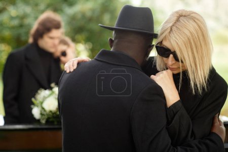 Foto de Dos personas abrazándose en la ceremonia funeraria al aire libre y vistiendo de negro - Imagen libre de derechos