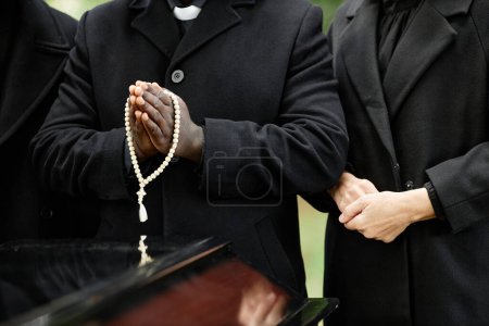 Foto de Primer plano de las personas vestidas de negro en la ceremonia funeraria al aire libre con enfoque en el rosario - Imagen libre de derechos