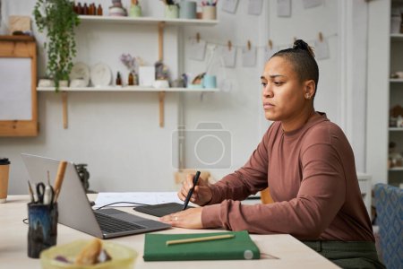 Foto de Retrato de vista lateral de una joven negra usando una tableta de lápiz mientras trabaja en nuevos diseños en el estudio, espacio para copiar - Imagen libre de derechos