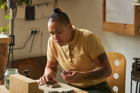 Téléchargez les photos : Portrait d'artisan femme tatouée créant des bijoux faits à la main dans un atelier confortable - en image libre de droit