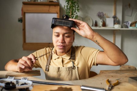Foto de Vista frontal del joyero femenino creando piezas de arte hechas a mano en una mesa de madera en un estudio rústico - Imagen libre de derechos